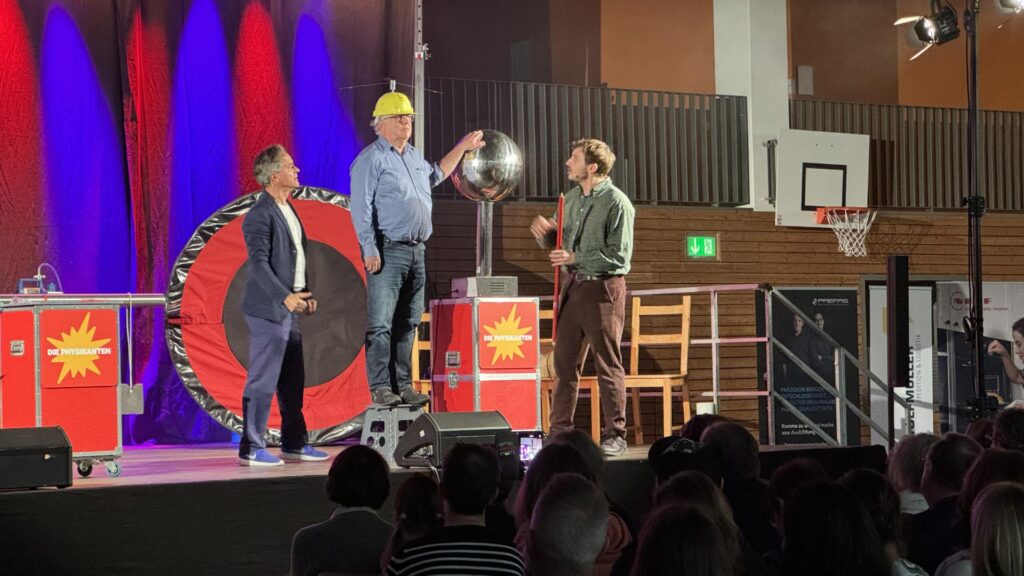 Bernhard Feineisen (Mitte), Leiter des Amtes für Bildung und Kultur, erlebt bei einem von Thomas Müller (links) und Felix Bold durchgeführten Experiment hautnah, wie 700.000 Volt einen kleinen Propeller auf seinem Helm in Bewegung setzen. Foto: Nina Tossenberger